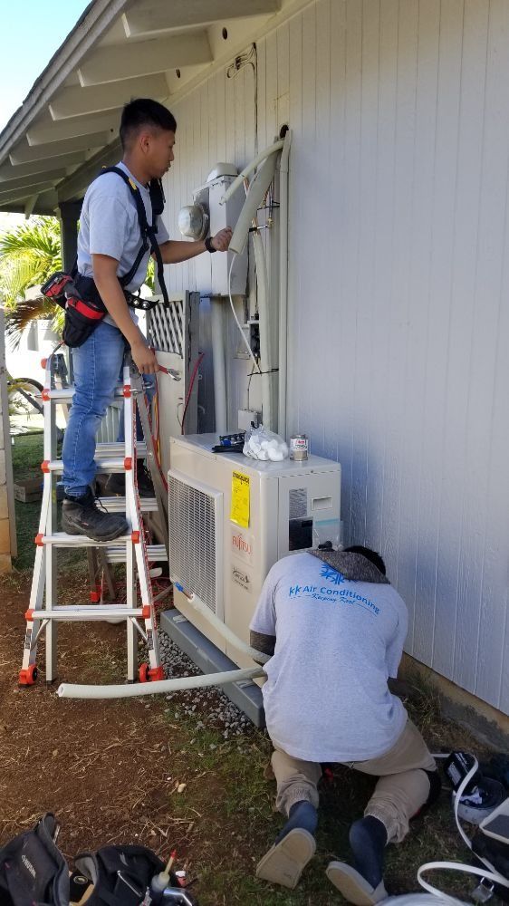 Two men are working on an air conditioner outside of a house.