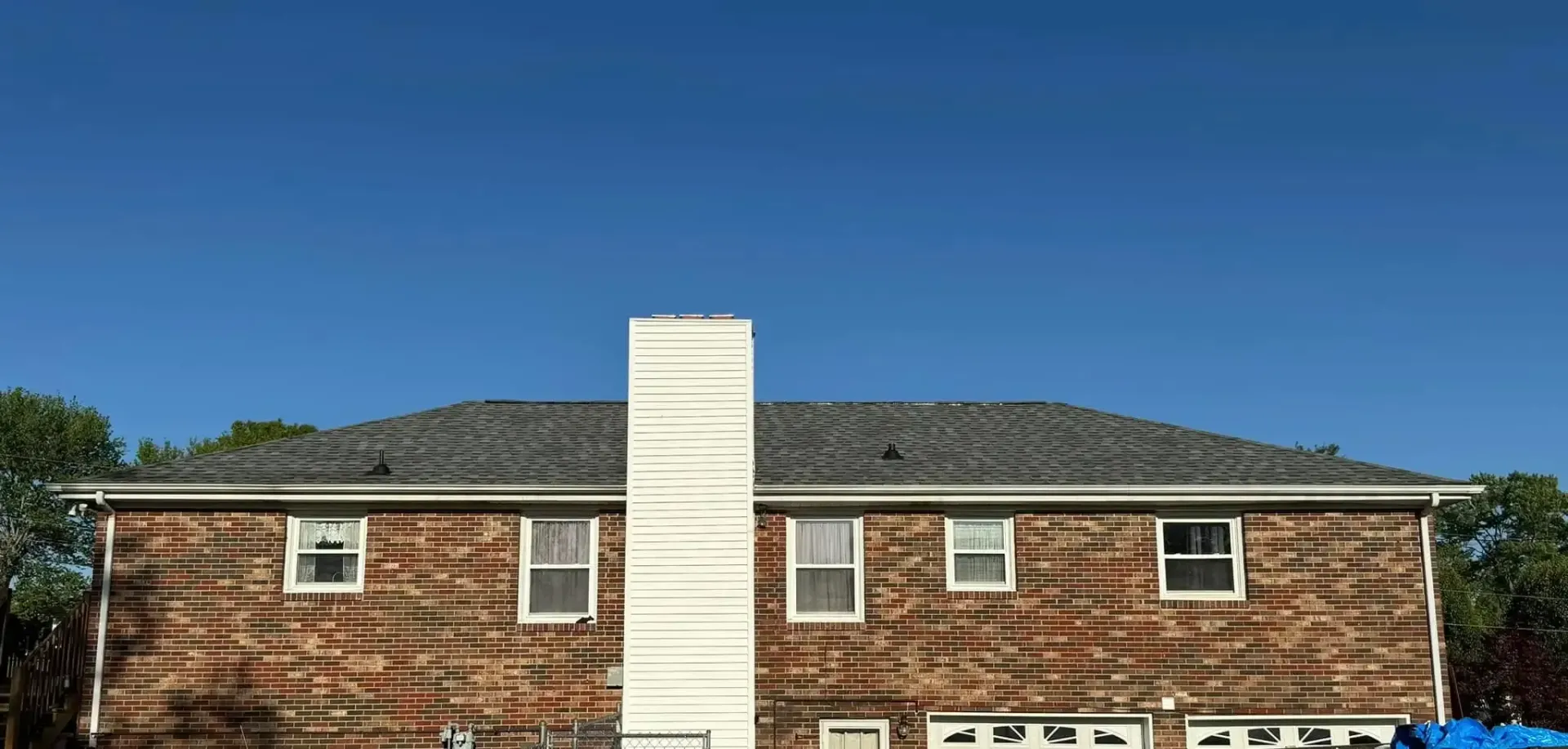 Two-story house with a chimney against a clear blue sky. Brown wood siding, gray roof, and white trim.