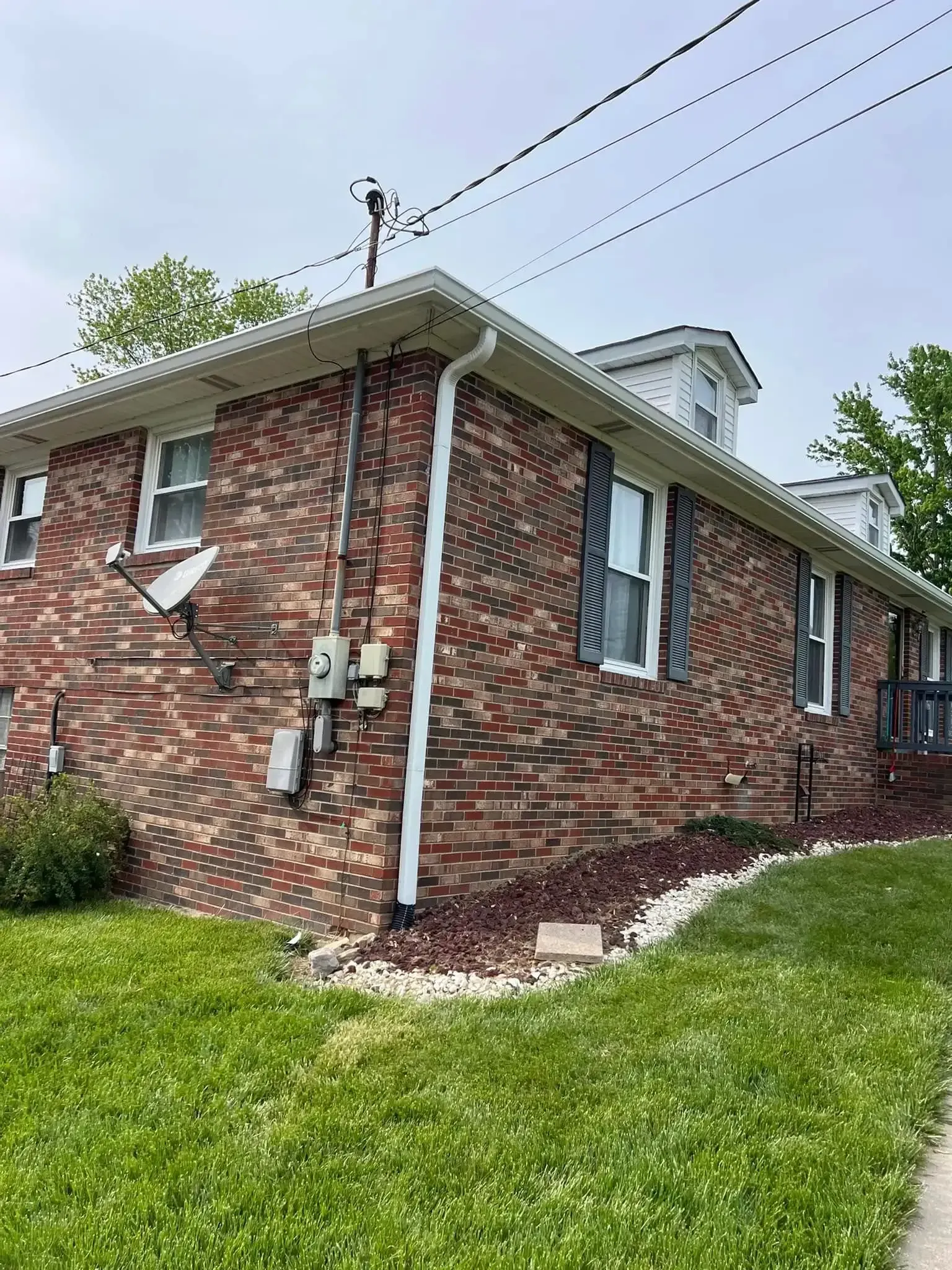 Brick building with white trim, windows, and dark shutters, under a cloudy sky.