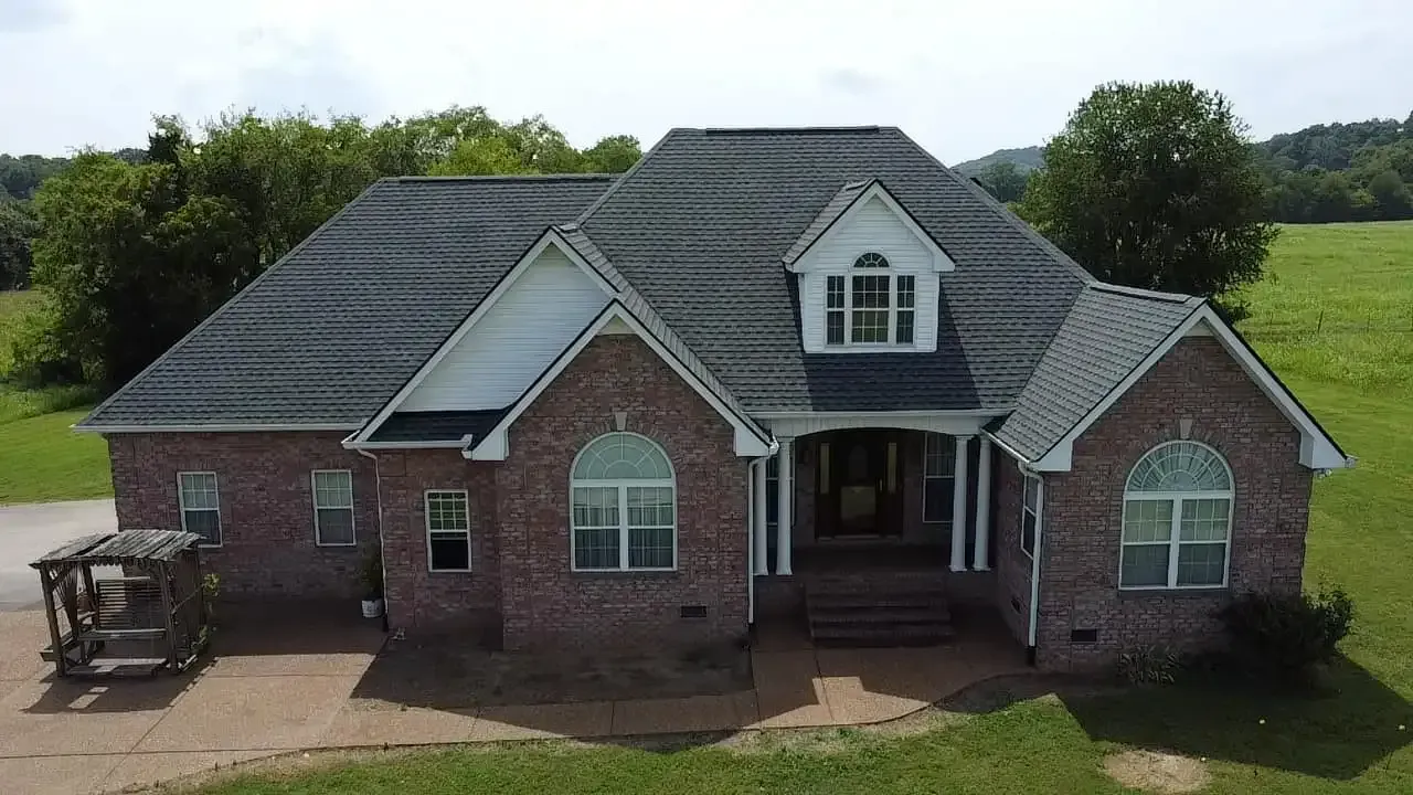 Brick house with white trim and a dark gray roof in a grassy field.
