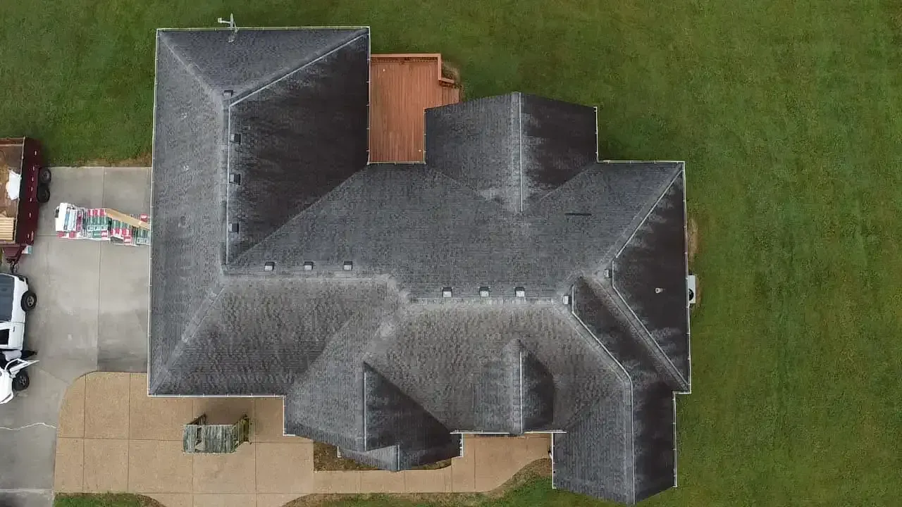 Aerial view of a house with a dark grey roof, brown deck, and green lawn. A white truck and debris sit in the driveway.