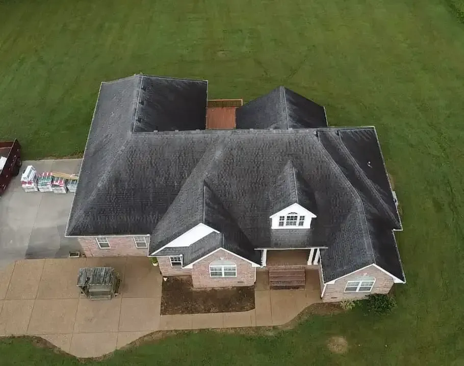 Overhead view of a brick house with a dark roof on a green lawn; a concrete driveway is in front.
