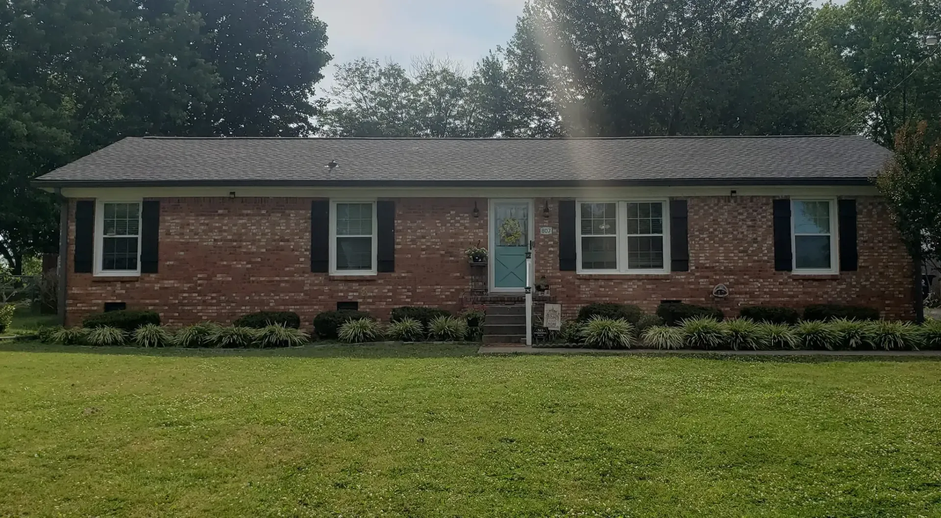 Brick ranch home with a blue door, black shutters, and a grassy lawn.