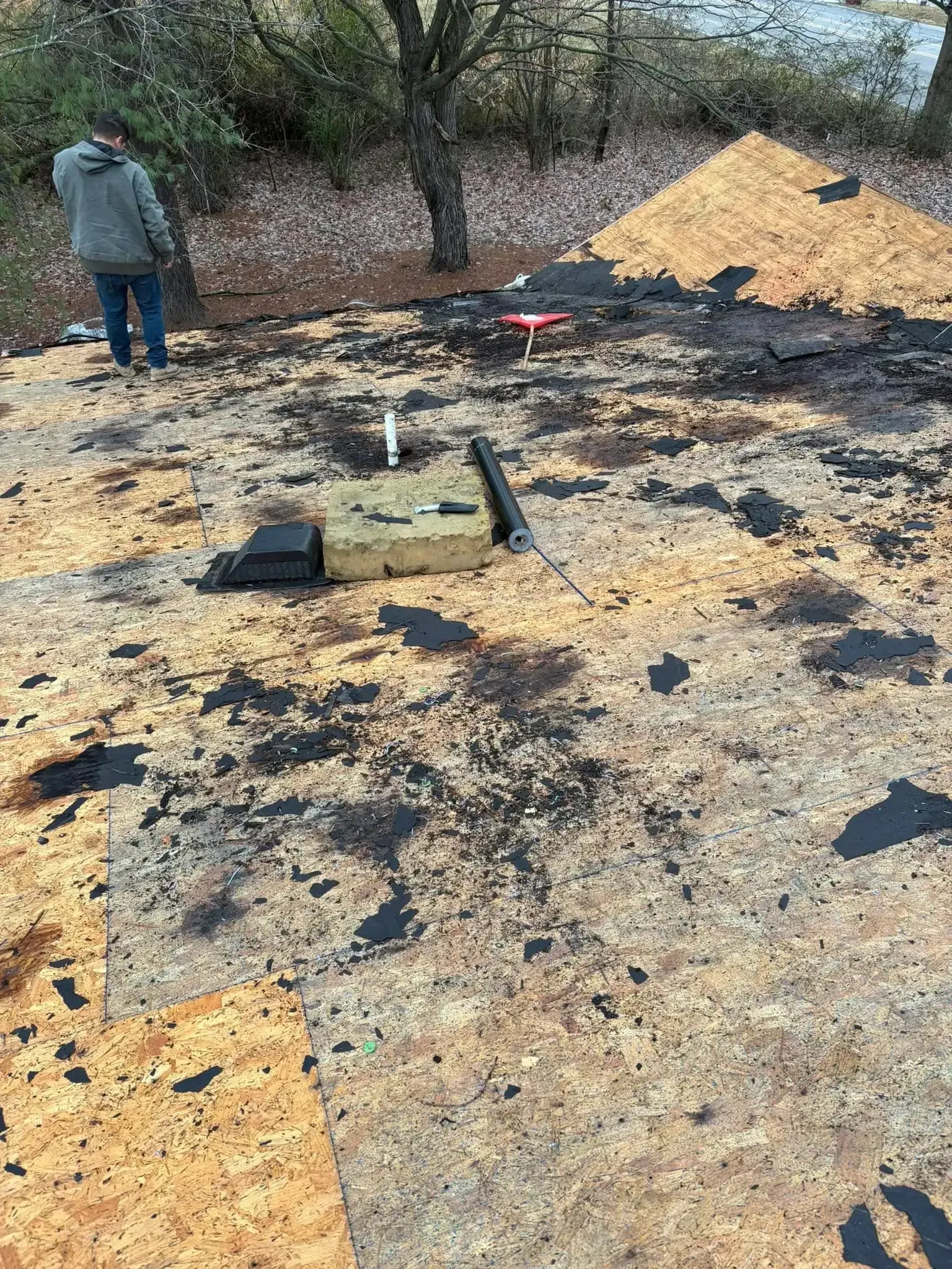 Person on a roof with materials, wood and black tar-like substances. Brown and yellow tones.