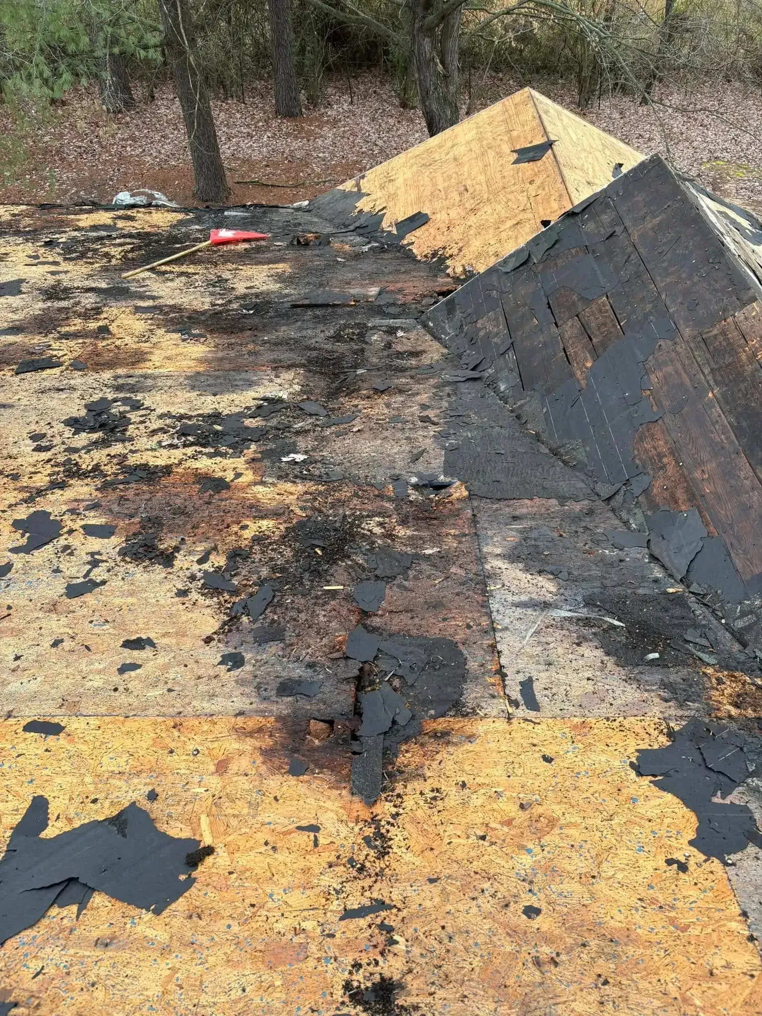 Damaged rooftop with missing shingles and exposed wood. Dark discoloration, possibly from fire or age.
