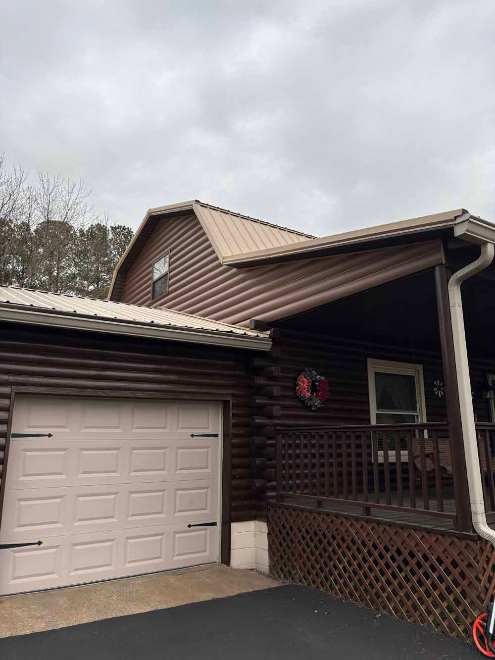 Brown log cabin with a garage and porch, brown metal roof, and a beige garage door.