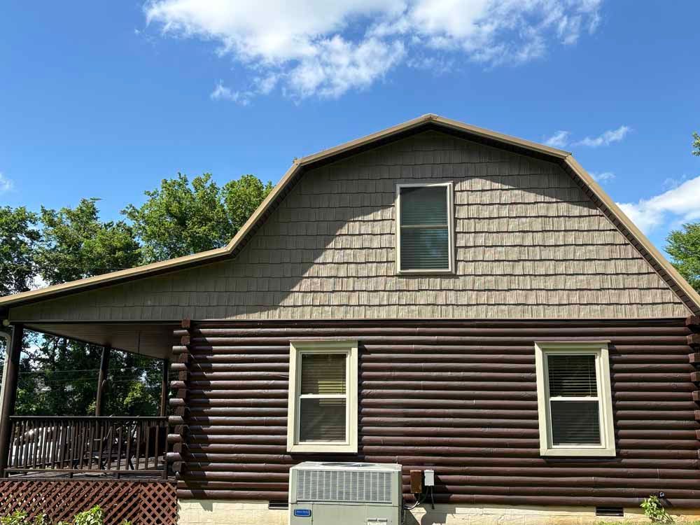 Brown log cabin with a covered porch, beige roof, and blue sky.