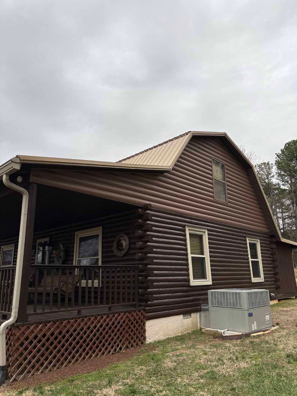 Brown log cabin with a metal roof, porch, and air conditioning unit on the grass.