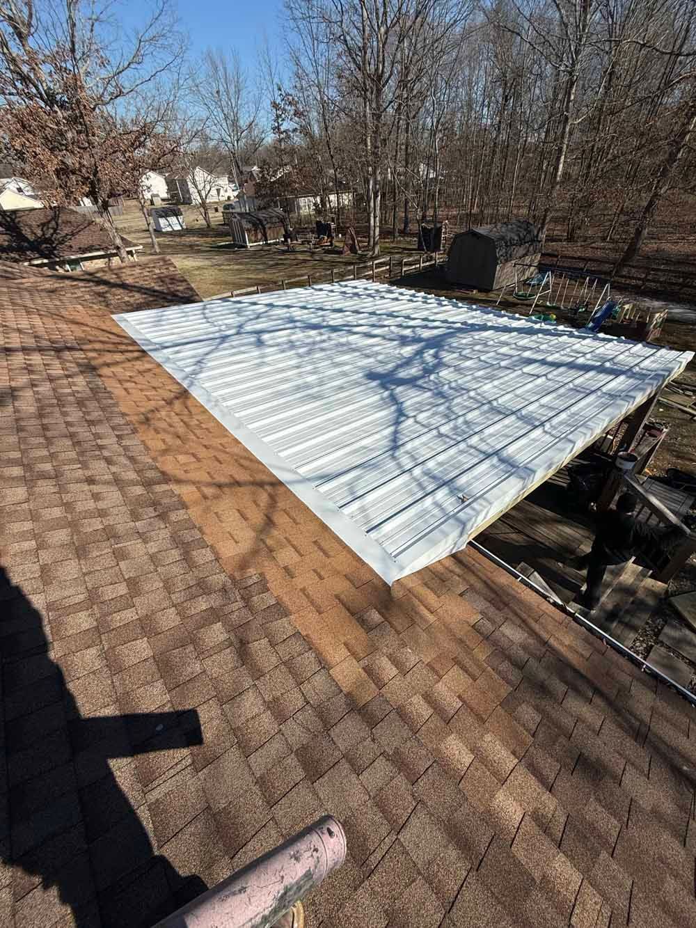 A white metal sheet on a brown shingled roof; sunlight casts shadows. Backyard setting.