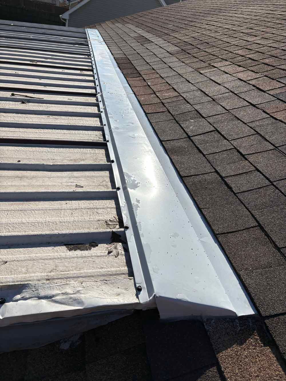 Metal flashing along the roof ridge, connected to shingles and a metal roof.