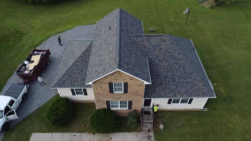 Overhead view of a house with a newly installed gray roof. Two workers by the house and truck.