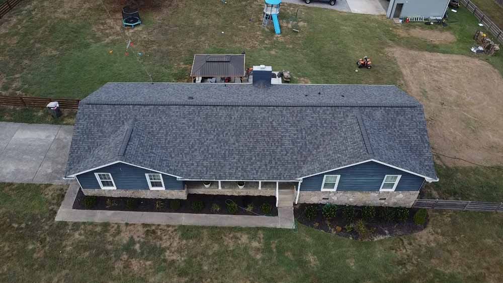 Overhead view of a blue-sided house with gray roof and stone facade; driveway in front.