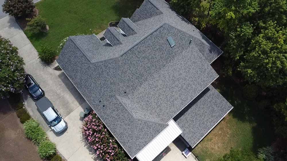 Overhead view of a gray-roofed house with a driveway and surrounding trees.