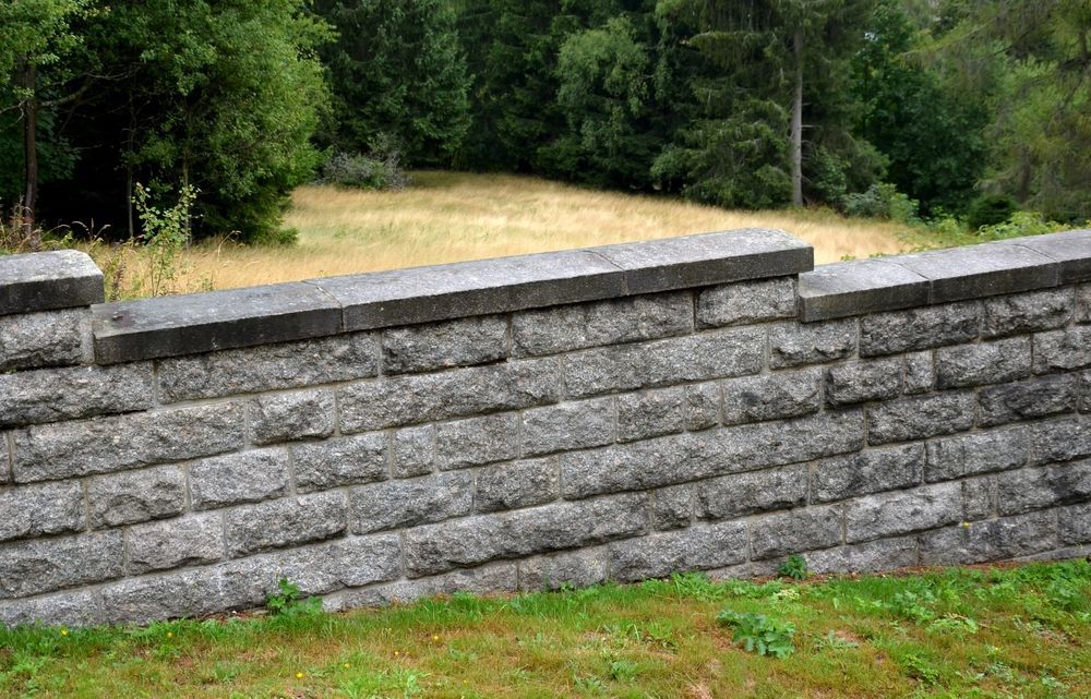 A Stone Wall Surrounds a Grassy Field With Trees in the Background — Wayne Hall Concreting in South Lismore, NSW