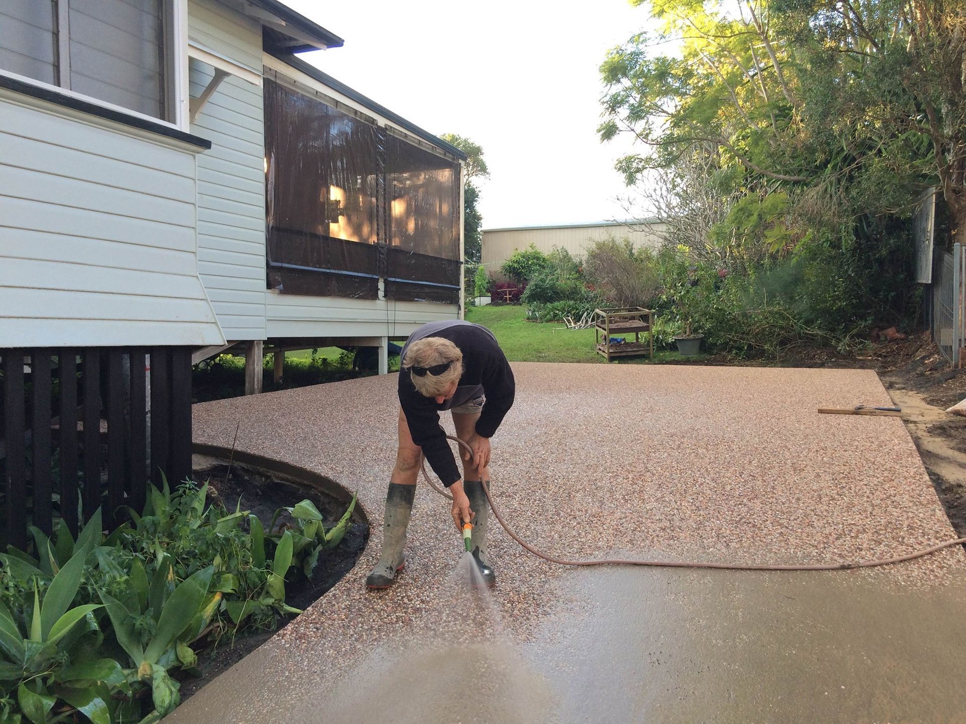A man is standing on a driveway hosing down the concrete — Wayne Hall Concreting in South Lismore, NSW