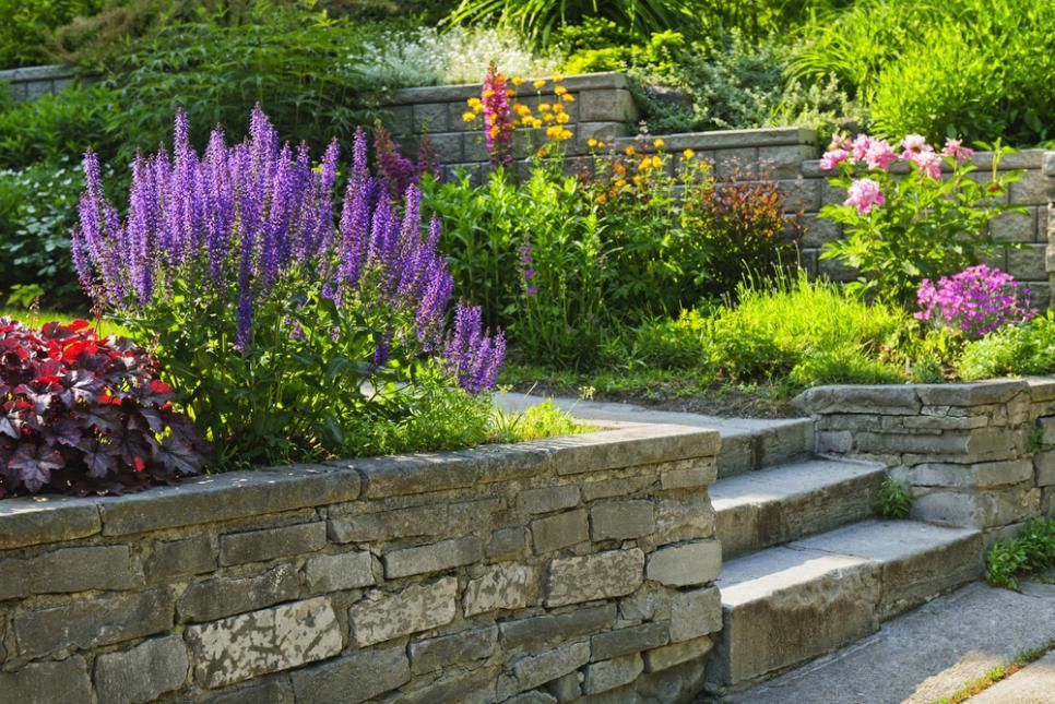 A Stone Wall Surrounds a Garden Filled With Lots of Flowers and Plants — Wayne Hall Concreting in South Lismore, NSW
