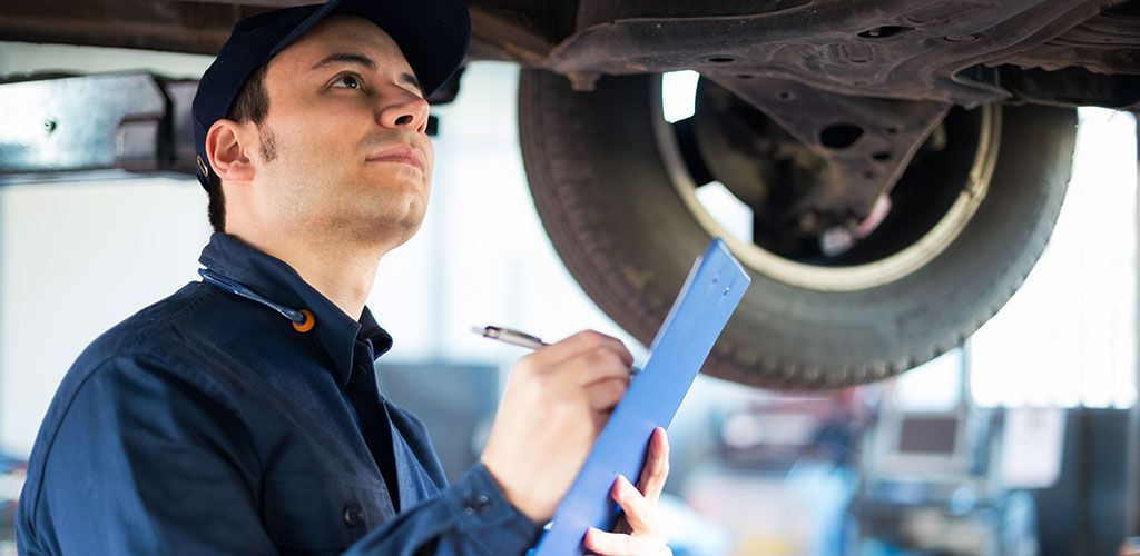 A Mechanic Is Writing On A Clipboard Under A Car β Coffs Harbour Automotive In Coffs Harbour, NSW
