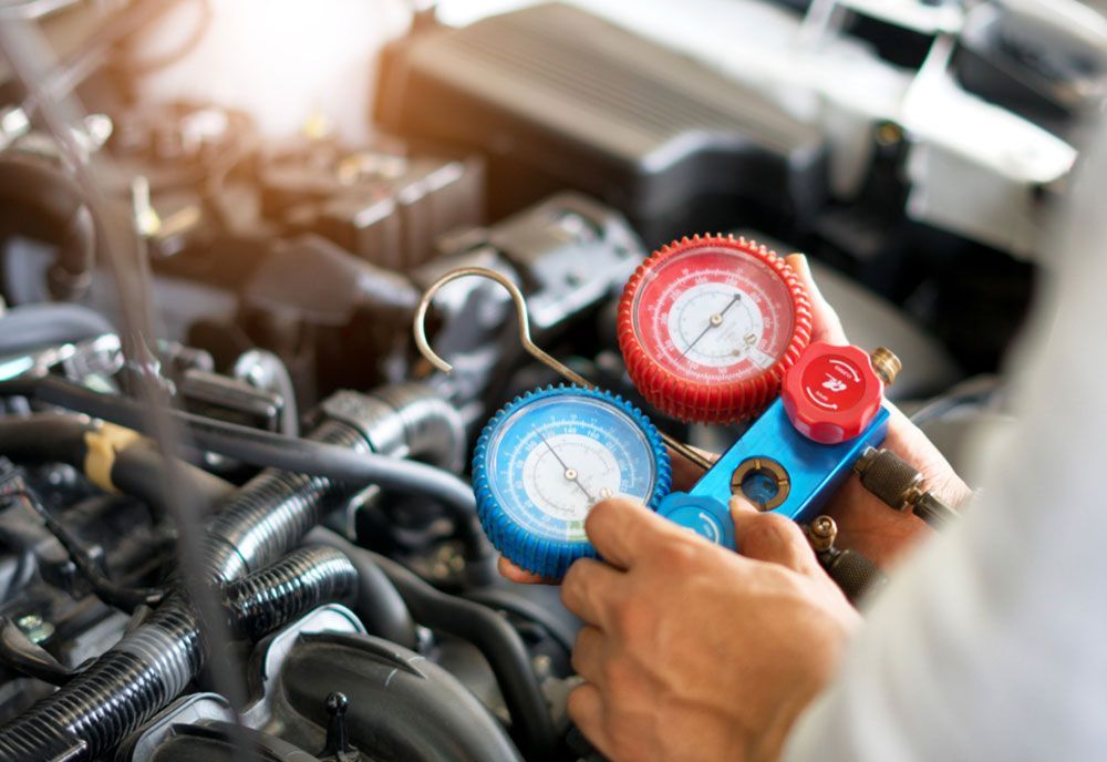 A Close Up Of A Person Holding A Gauge In Front Of A Car Engine — Coffs Harbour Automotive In Coffs Harbour, NSW