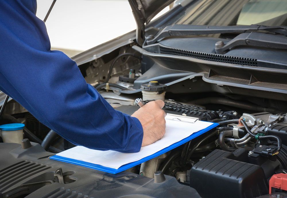 A Mechanic Is Writing On A Clipboard Under The Hood Of A Car — Coffs Harbour Automotive In Coffs Harbour, NSW