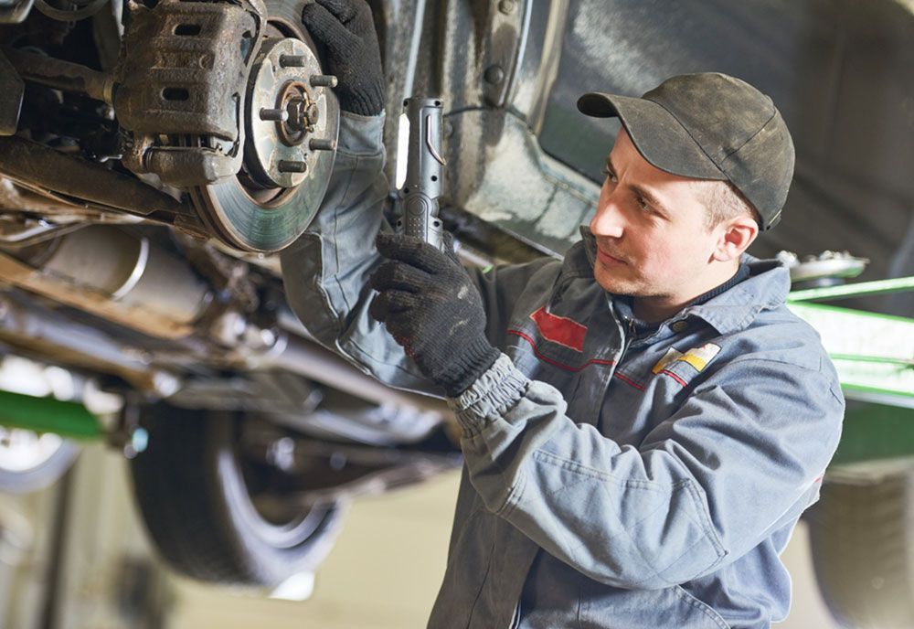 A Man Is Working On The Underside Of A Car In A Garage — Coffs Harbour Automotive In Coffs Harbour, NSW