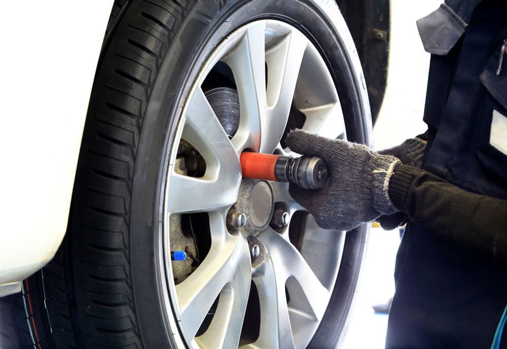A Person Is Changing A Tire On A Car With A Wrench — Coffs Harbour Automotive In Coffs Harbour, NSW