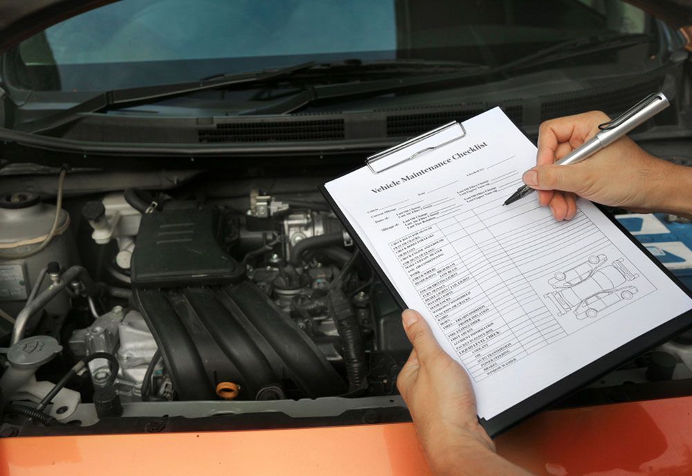 A Person Is Writing On A Clipboard In Front Of A Car Engine — Coffs Harbour Automotive In Coffs Harbour, NSW