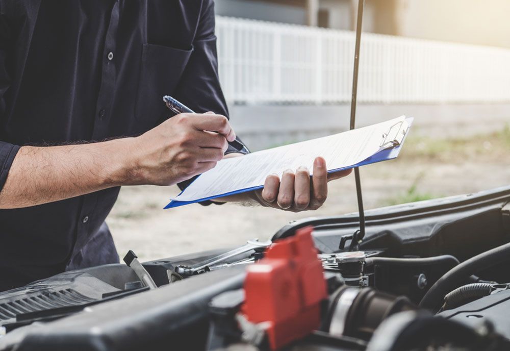 A Man Is Writing On A Clipboard While Standing Next To A Car — Coffs Harbour Automotive In Coffs Harbour, NSW