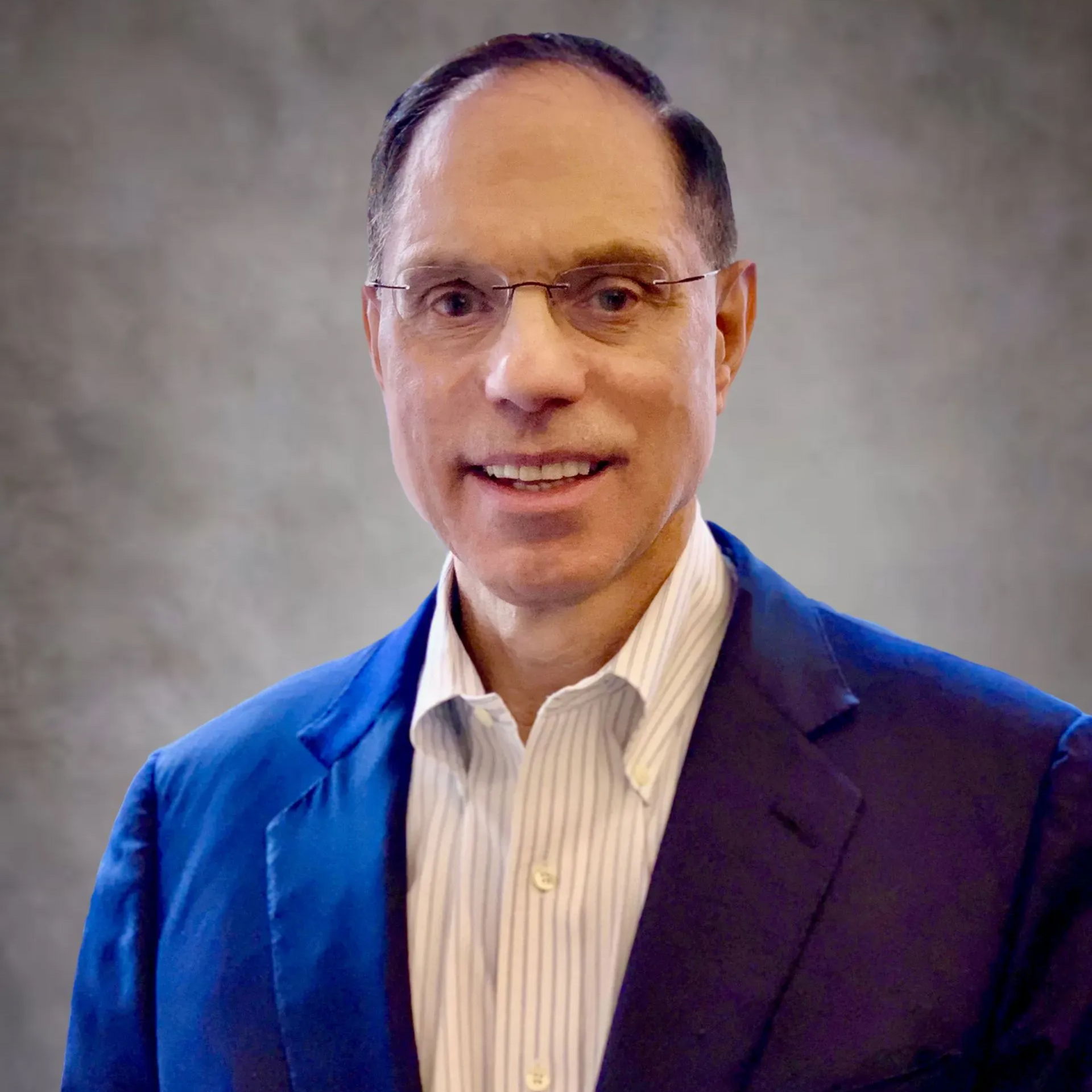 Man in blue blazer and glasses smiles, indoors.