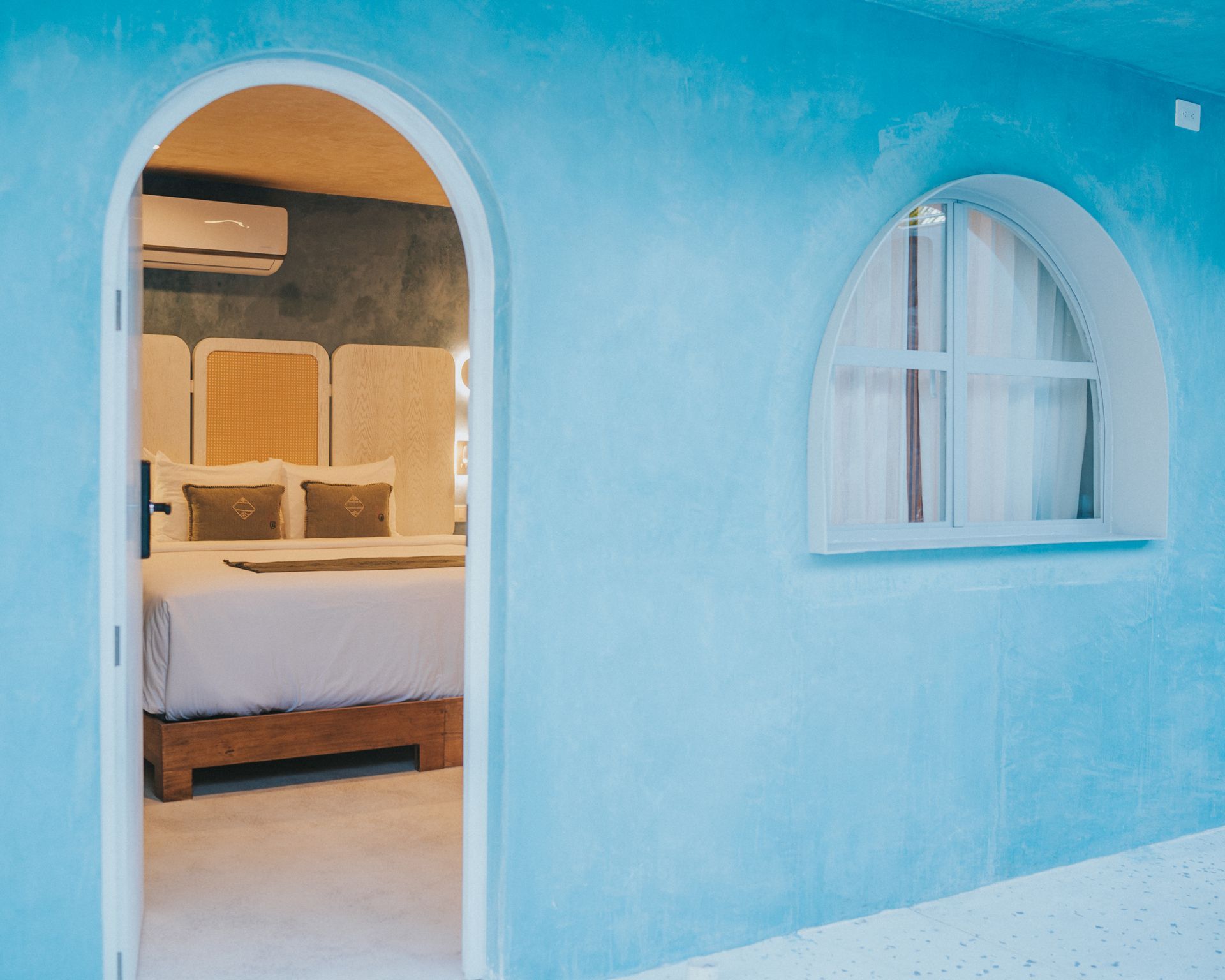 Una habitación de paredes azules con una puerta arqueada que conduce a un dormitorio con una cama y una ventana.