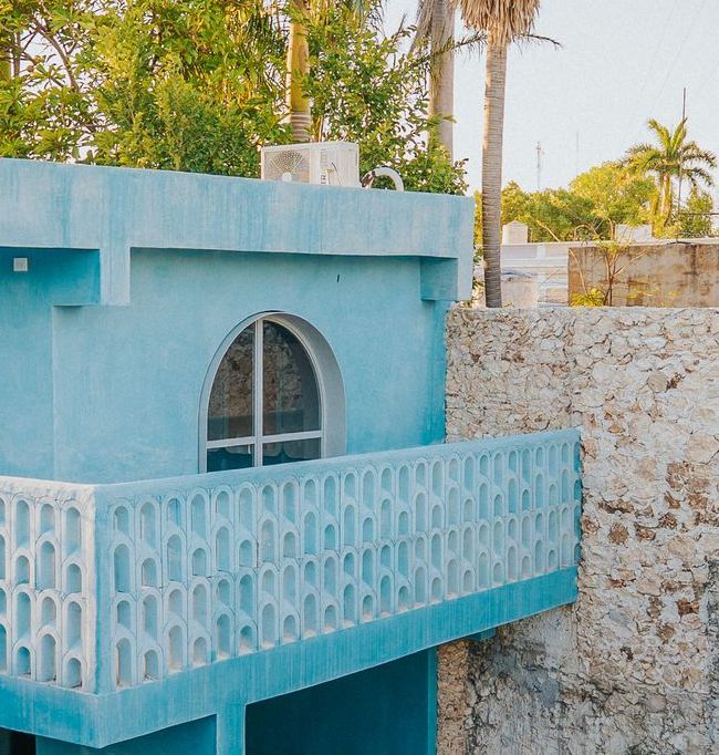 Edificio de estuco azul con ventana arqueada y balcón decorativo.