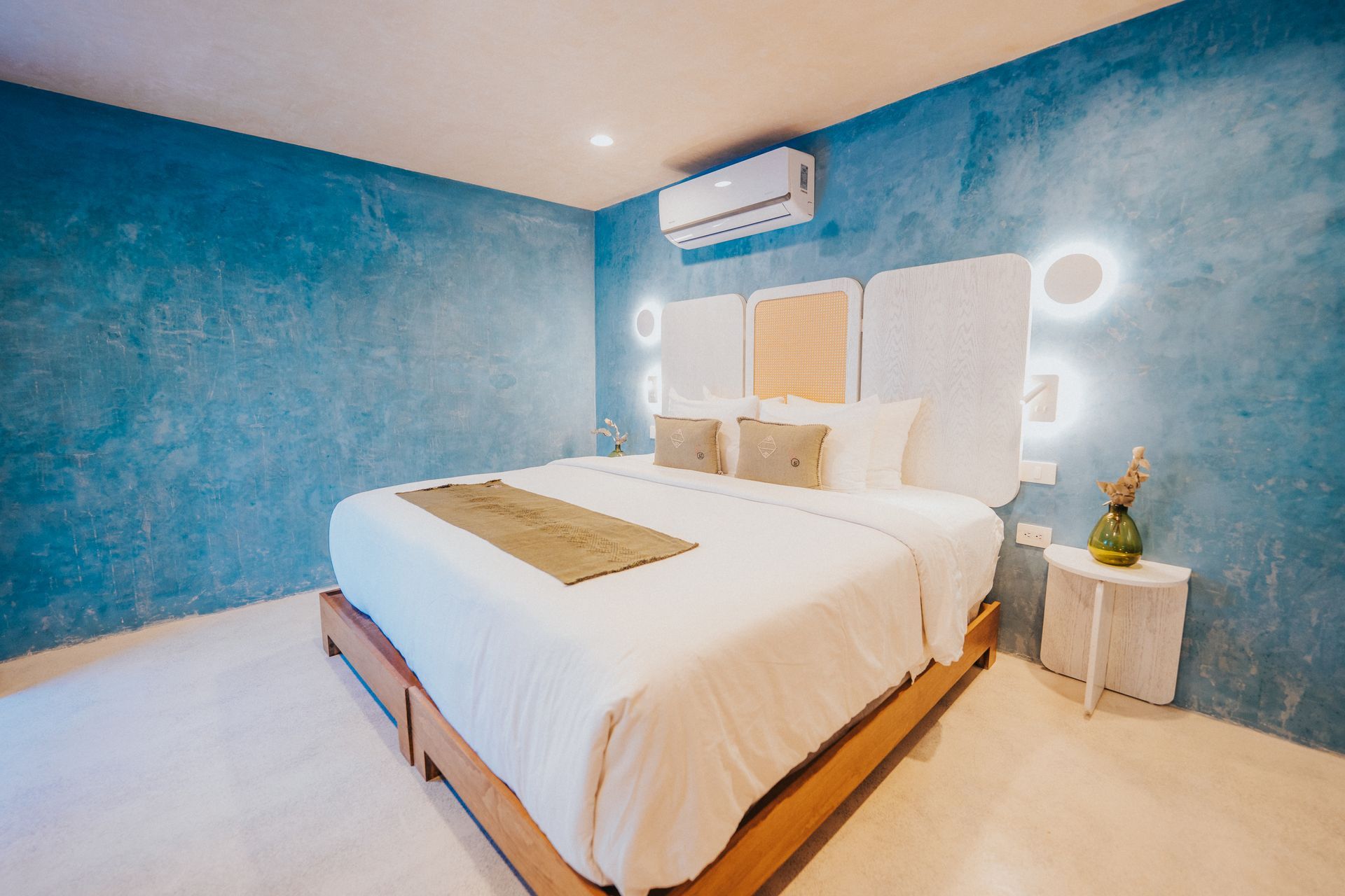 Dormitorio con paredes con textura azul, ropa de cama blanca y cabeceras redondas iluminadas.