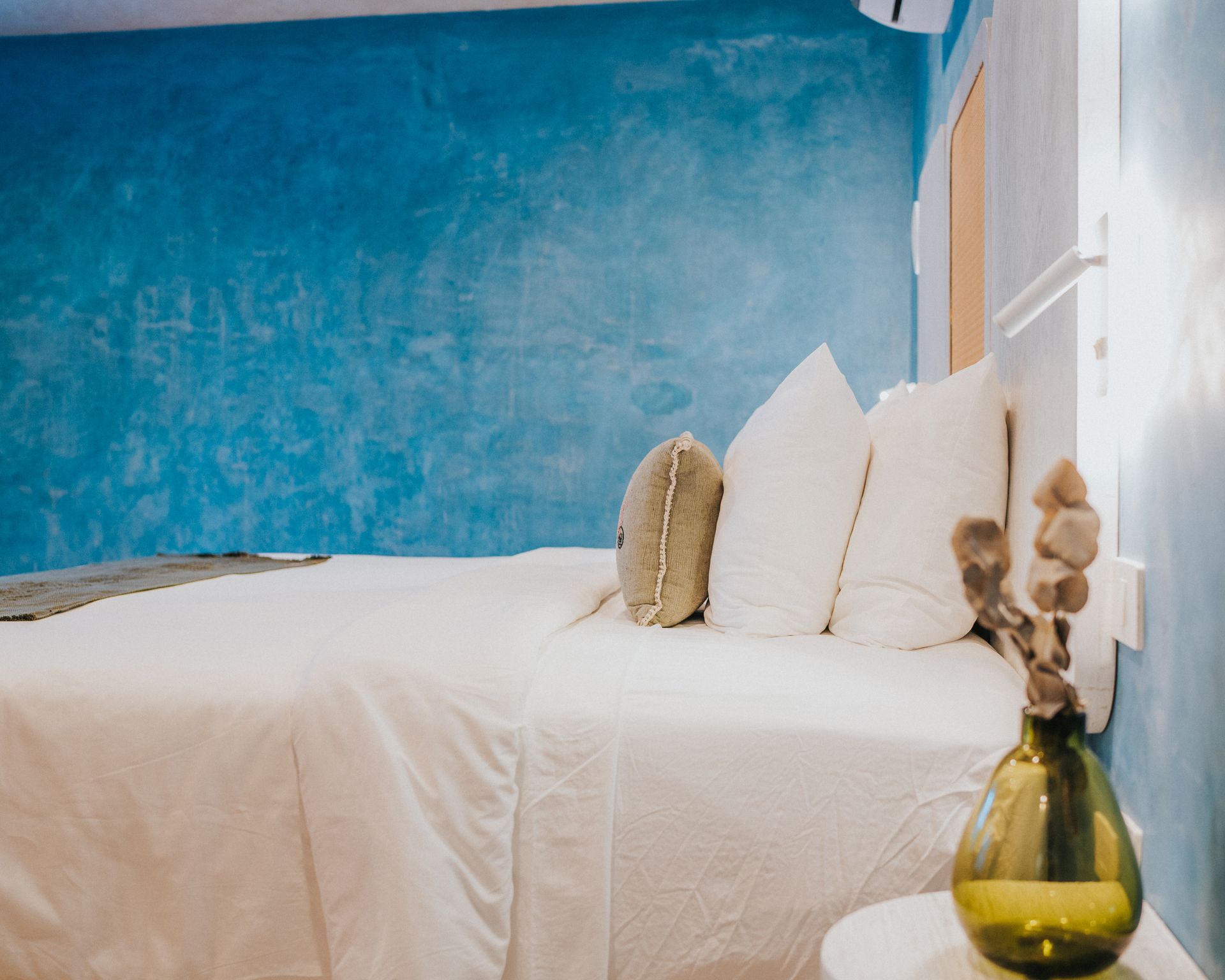 Dormitorio con cama blanca, pared azul y jarrón decorativo.