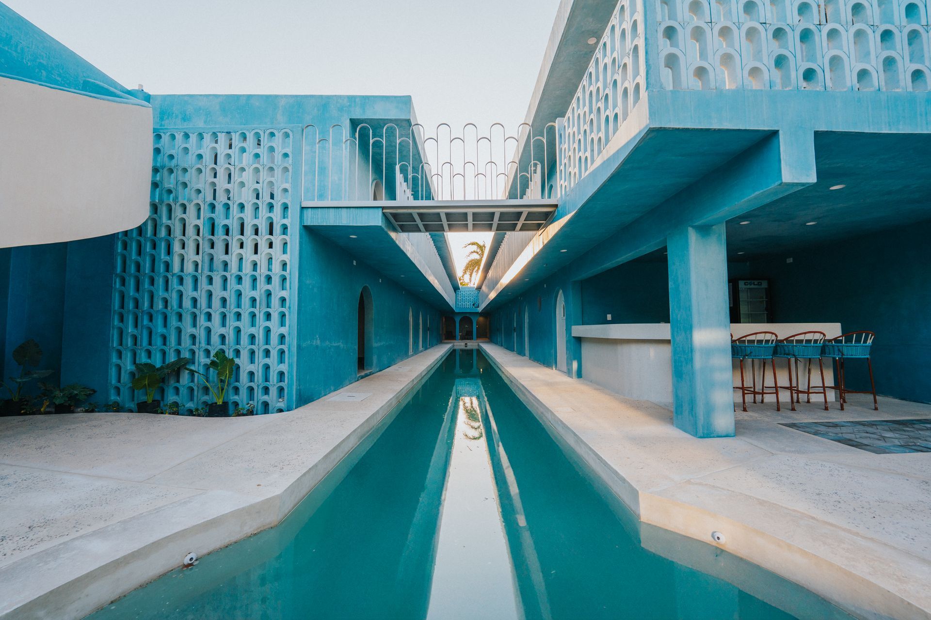 Edificio modernista azul con piscina larga, pasarela y bar al aire libre.