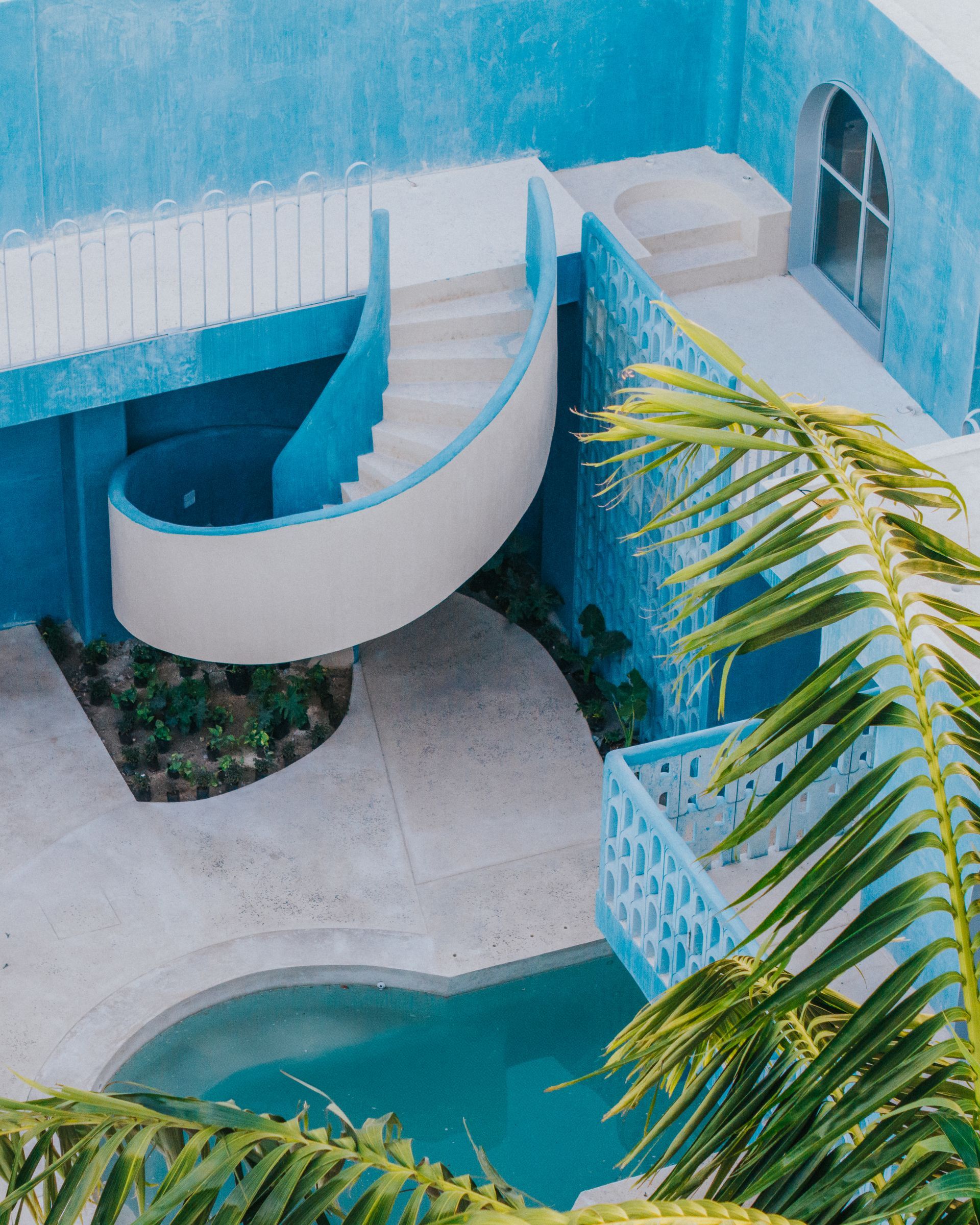 Exterior azul de edificio con escalera curva, con vistas a una piscina, con hojas de palmera.