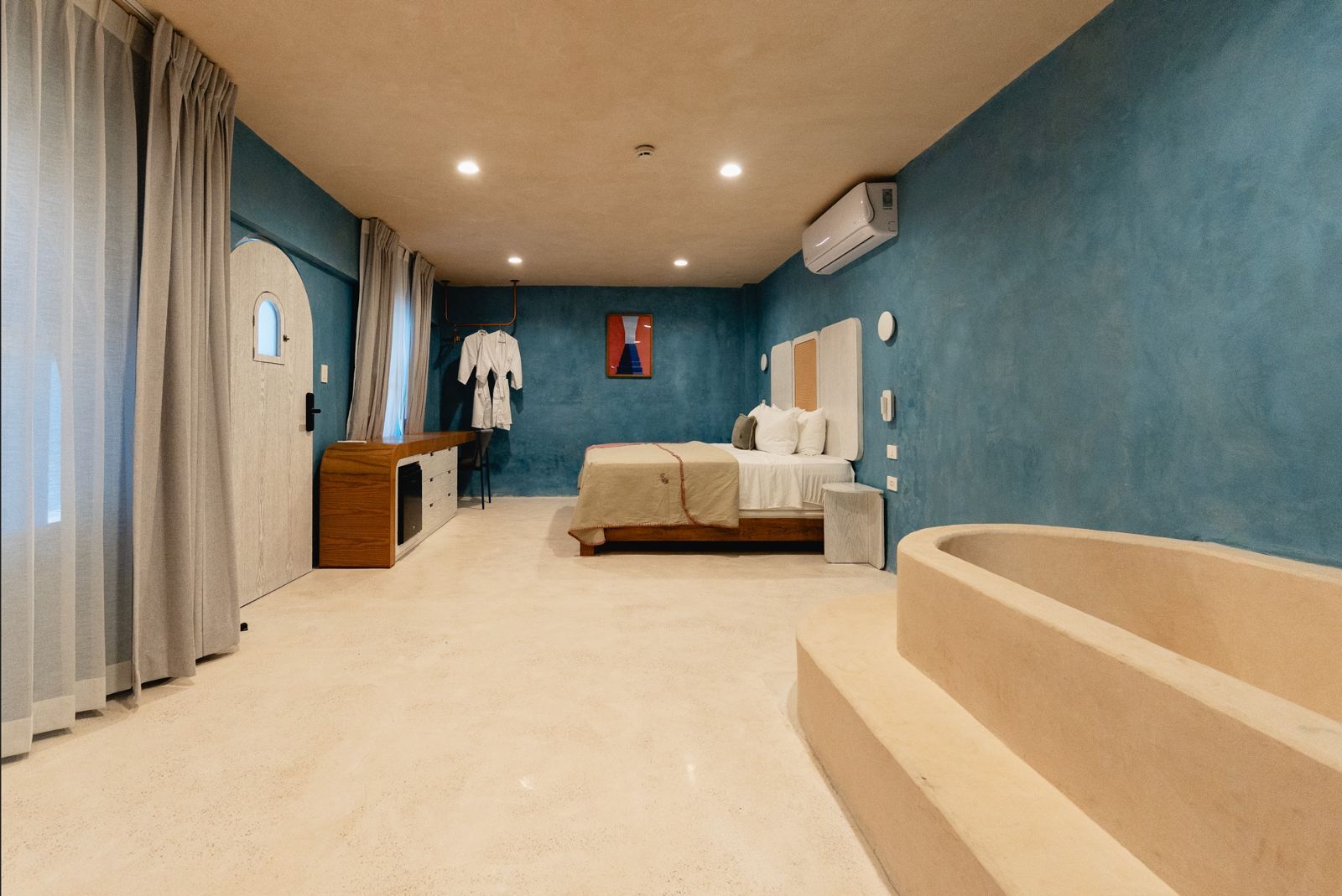 Habitación de hotel con paredes azules, suelo beige, cama king y jacuzzi.