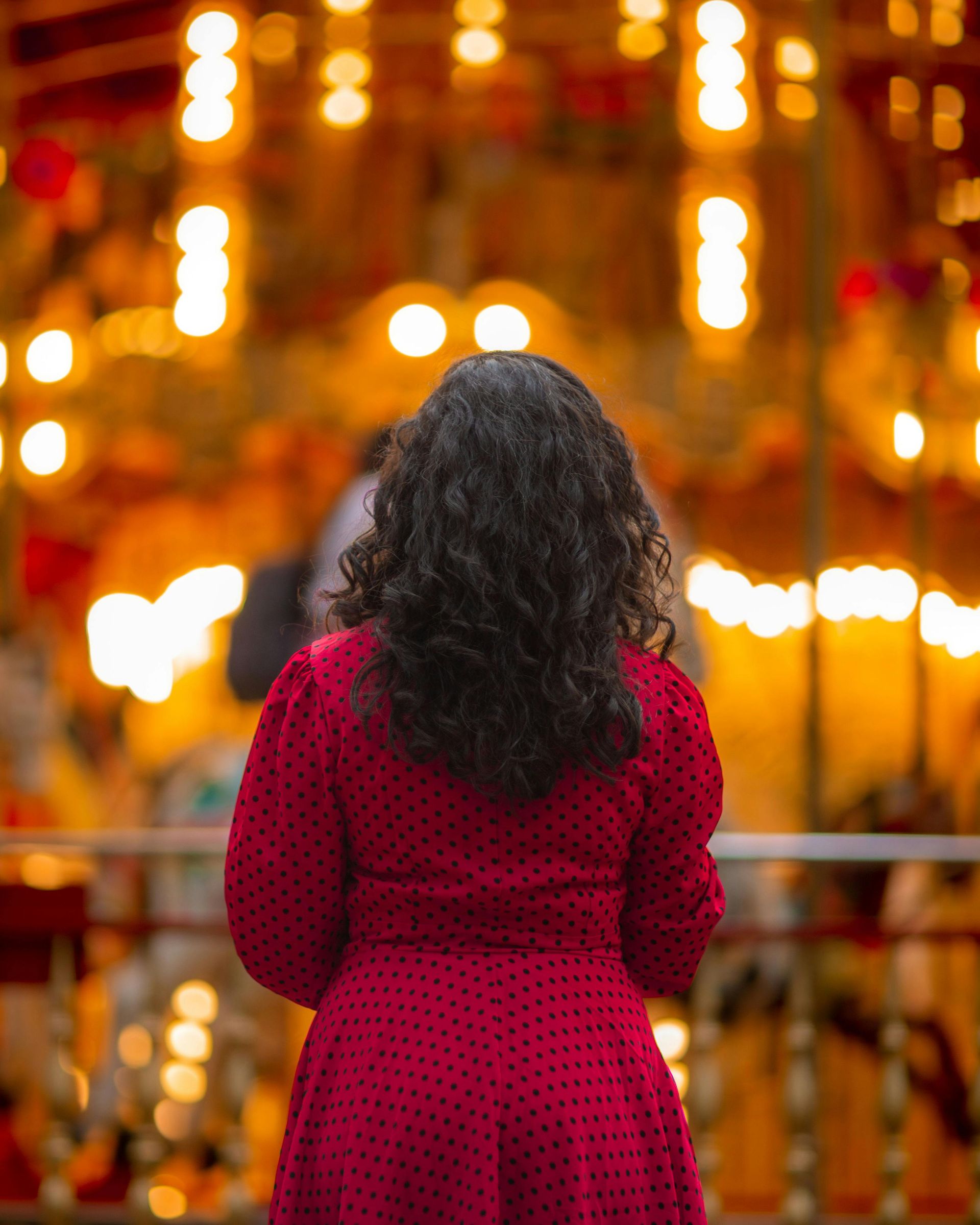 Mujer con vestido rojo frente a un carrusel con luces borrosas.