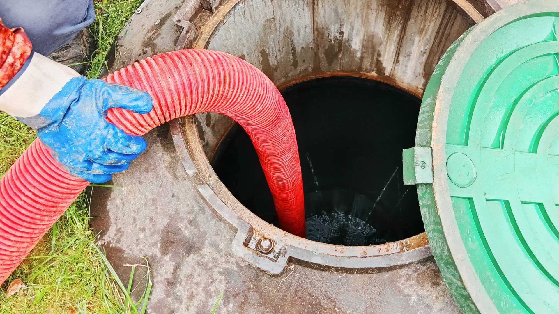 Technician inserting red hose into septic tank during septic system repair and cleaning.