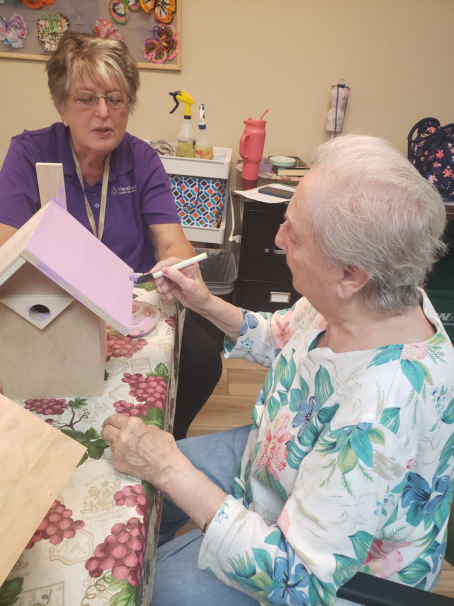 A woman is painting a birdhouse for an elderly woman.