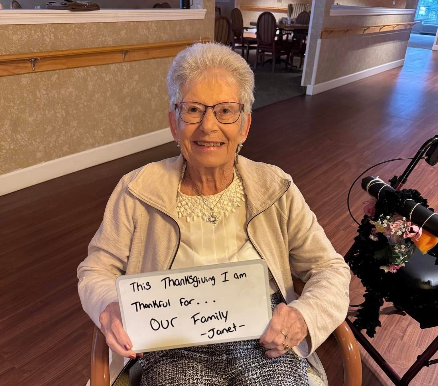 An elderly woman is holding a sign that says this thanksgiving i am thankful for our family