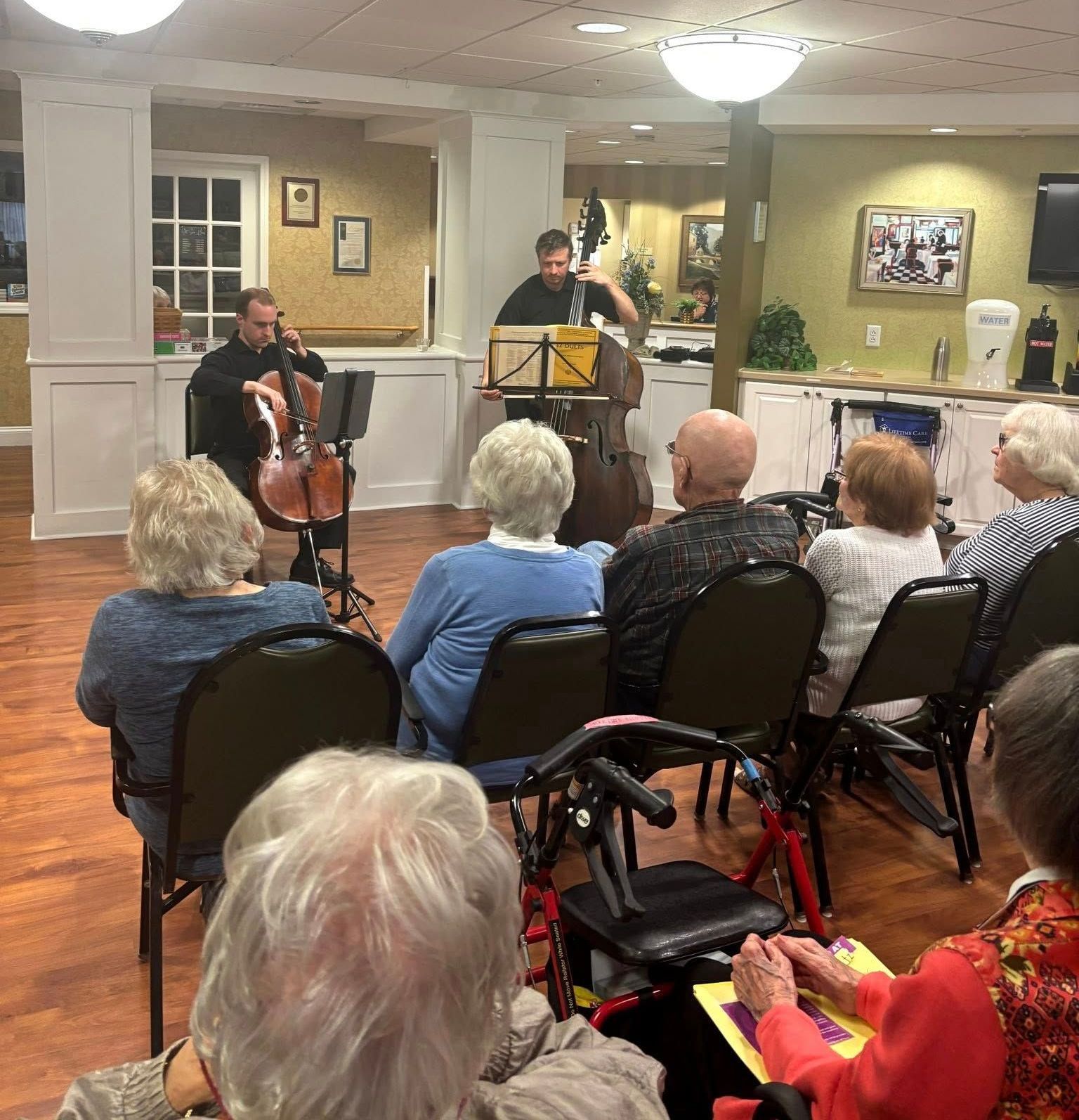 A group of people are sitting in chairs watching a man play a cello