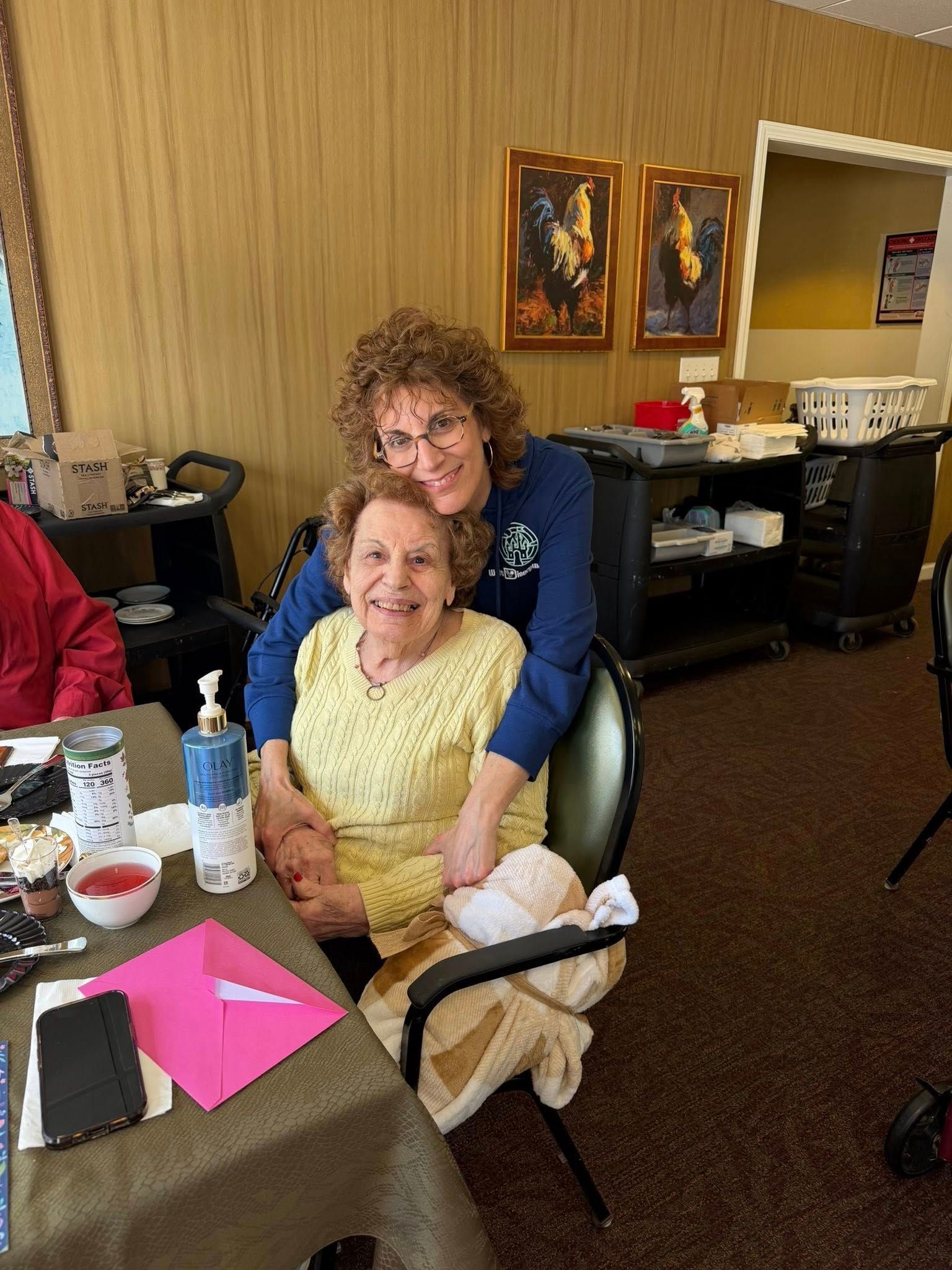 Two people smiling at a table in a room, with papers, drinks, and a purse in the foreground.