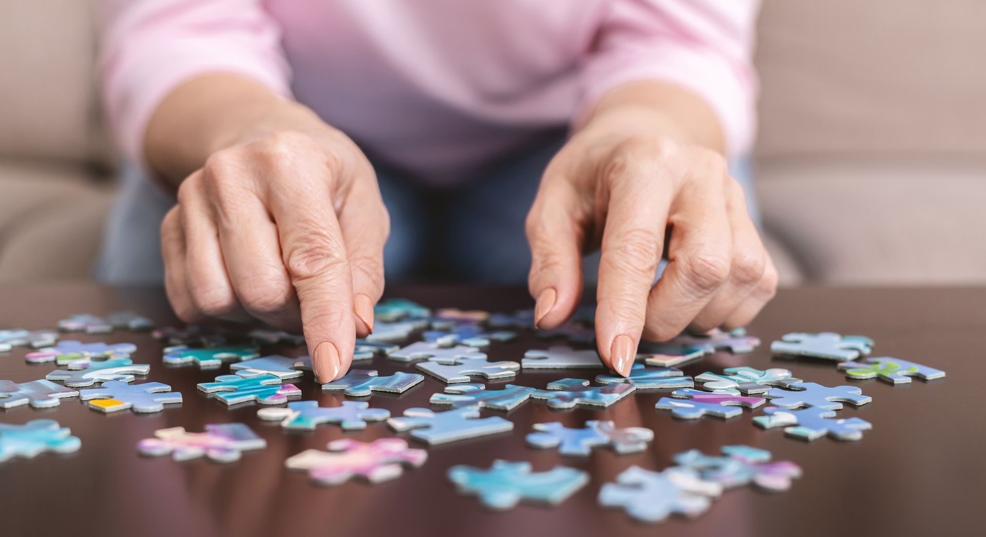 Hands working on a jigsaw puzzle on a dark wooden table.