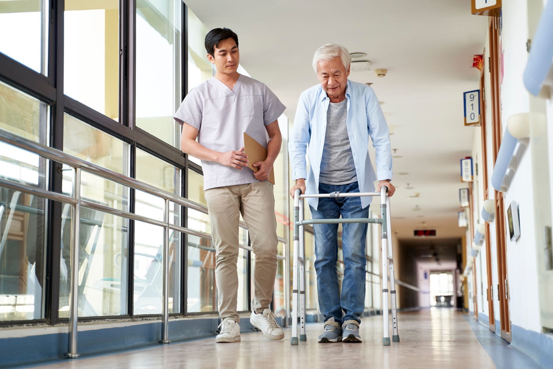 A nurse is helping an elderly man with a walker in a hospital hallway.