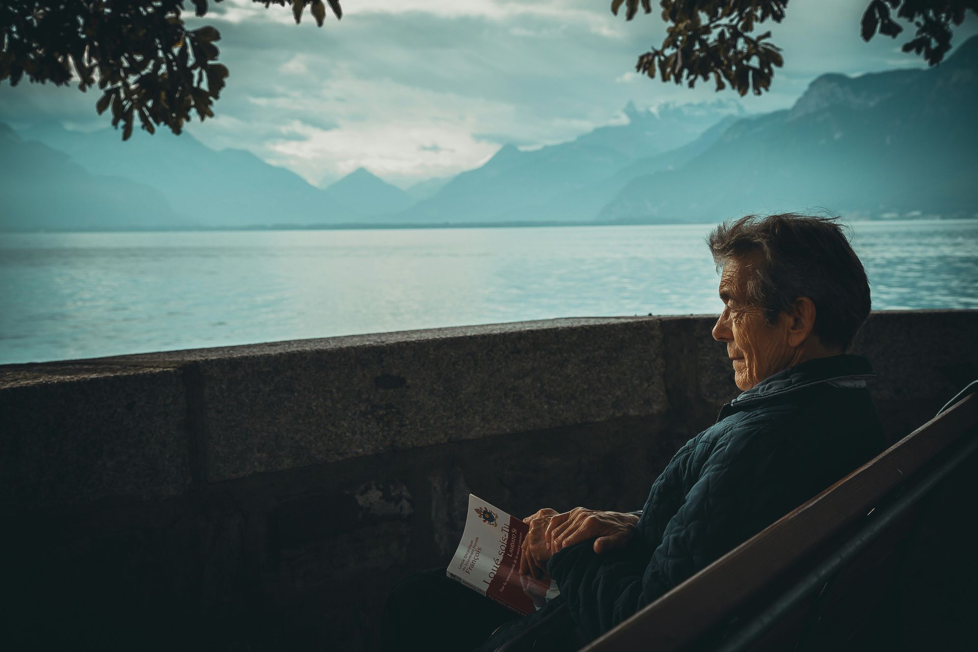 old man sitting by the water reading a book