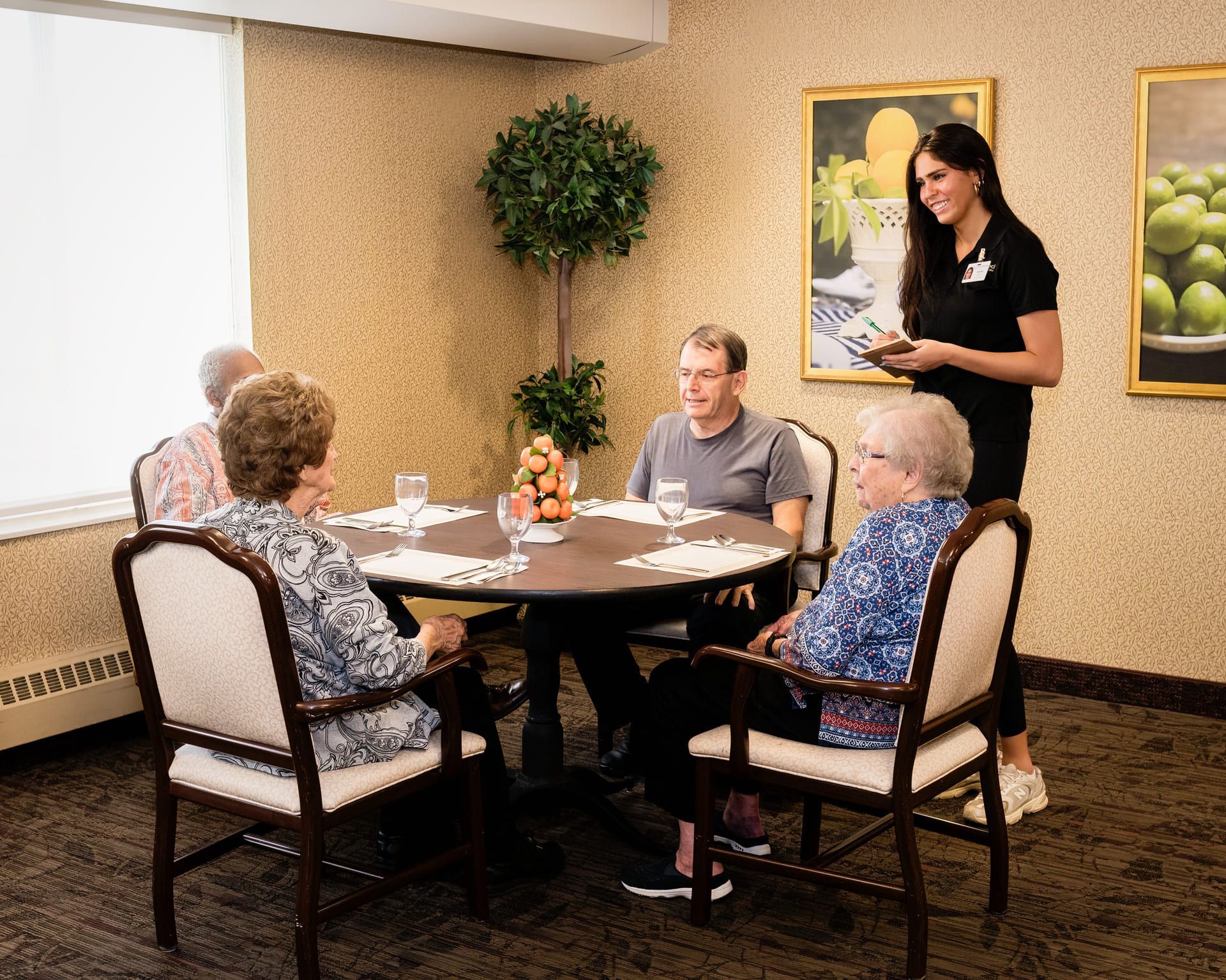 assisted living patients seated at a round table, served by a staff member