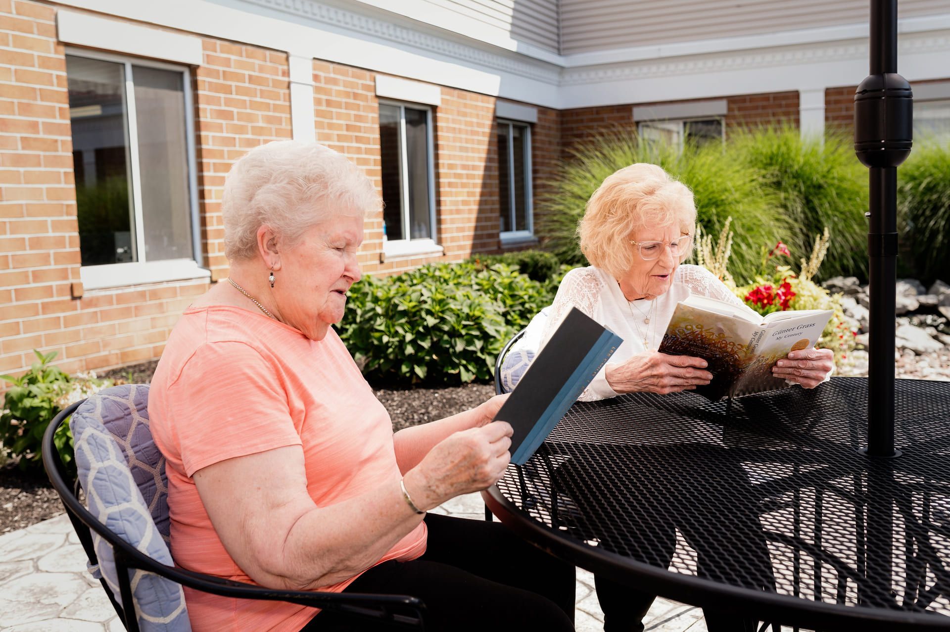 Two older women are sitting at a table reading books.