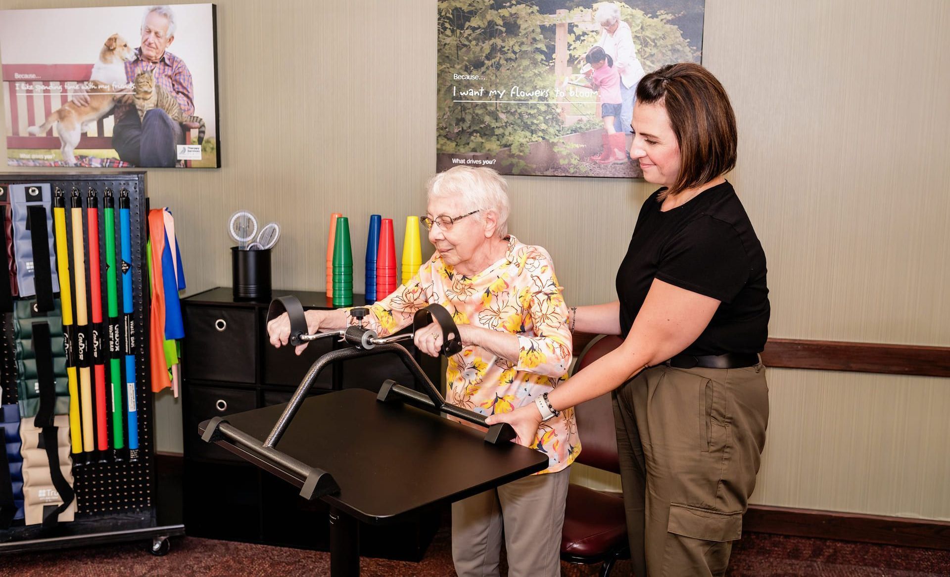 A woman is helping an elderly woman do exercises on a machine as occupational therapy. 