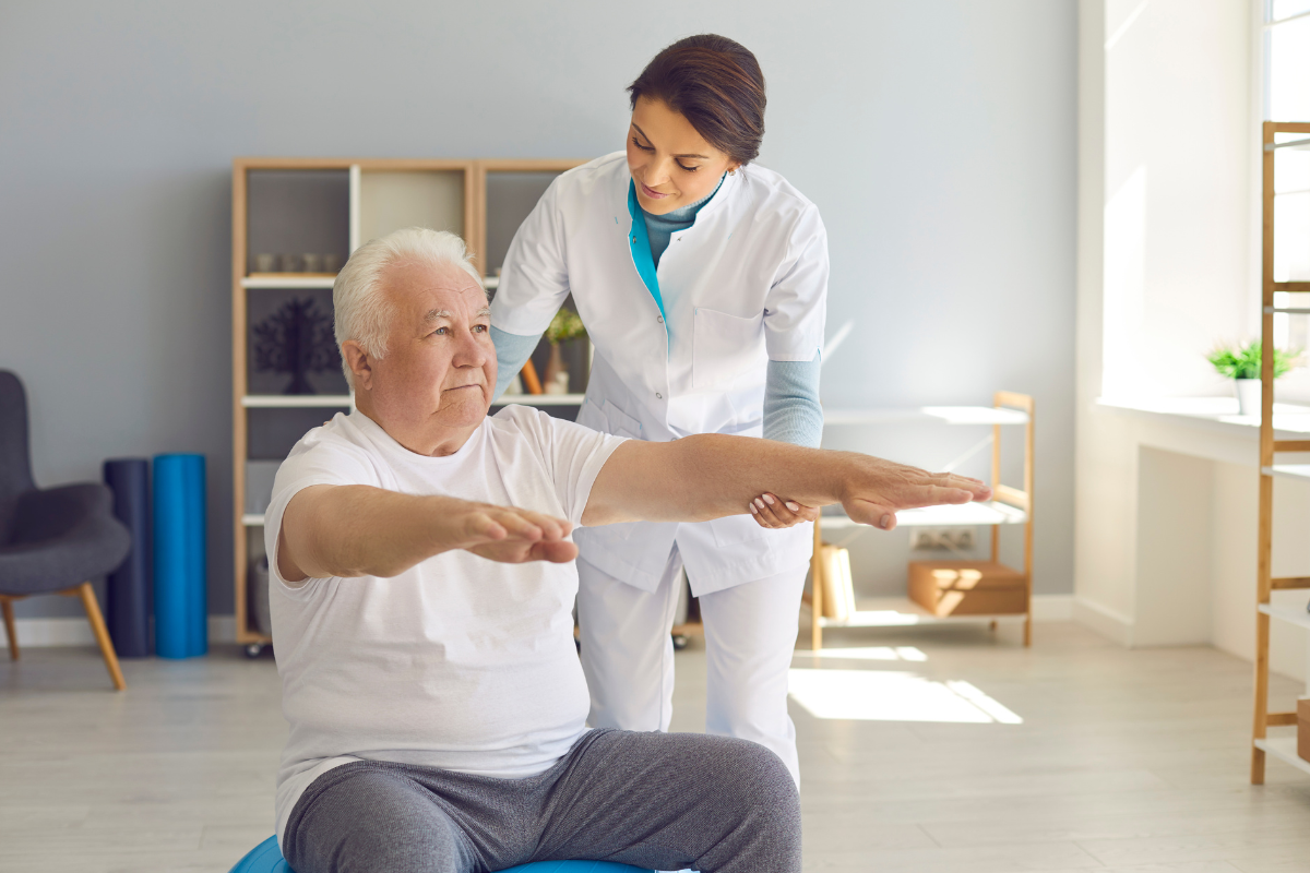 a nurse is helping an elderly man do exercises on a ball as part of geriatric physical therapy