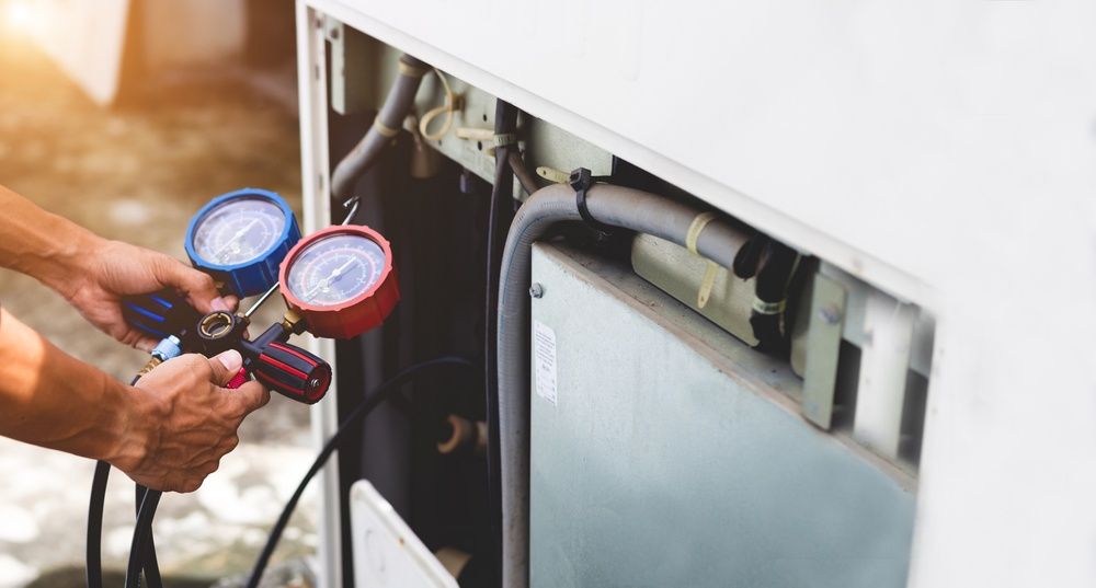 A Man is Working on an Air Conditioner With Two Gauges — Elements Air & Refrigeration In Cairns City, QLD