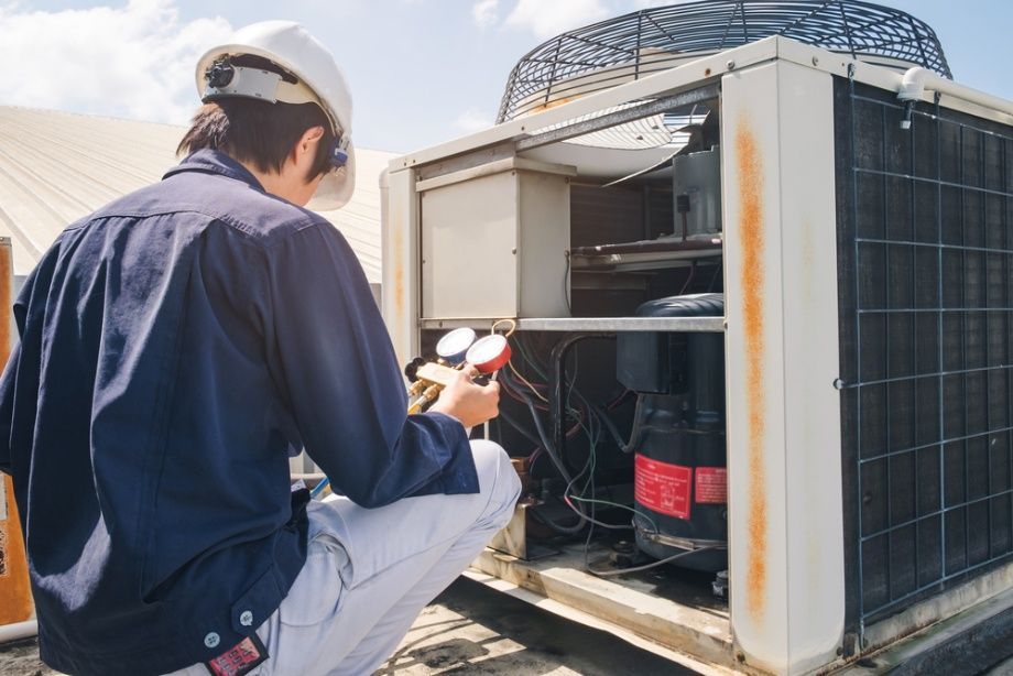 A Man is Kneeling Down in Front of an Air Conditioner — Elements Air & Refrigeration In Westcourt, QLD